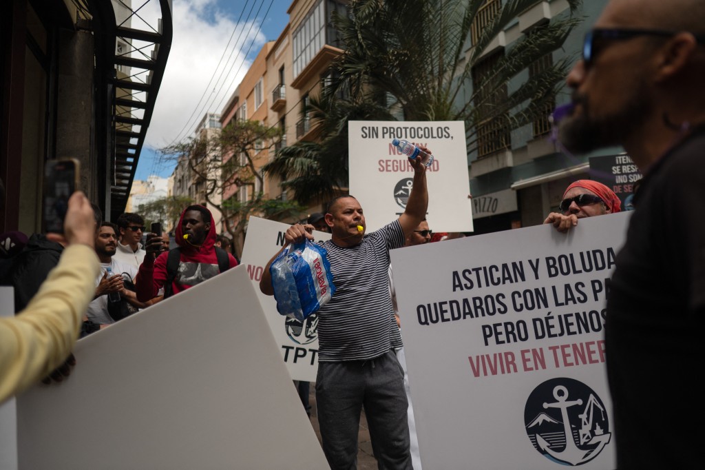 Photo by JORGE GUERRERO / AFP  Dockers hold banners reading 'Without protocol, no safety' as they protest against the arrival of a cruise ship affected by hantavirus in Santa Cruz de Tenerife on May 8, 2026.