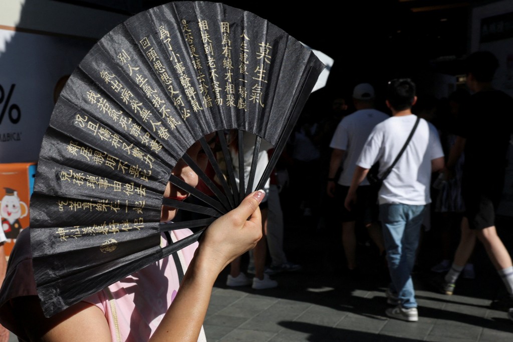 A person holds up a fan to cover her face from sunlight amid a yellow alert for heat, in Shanghai, China July 4, 2025. (Reuters)