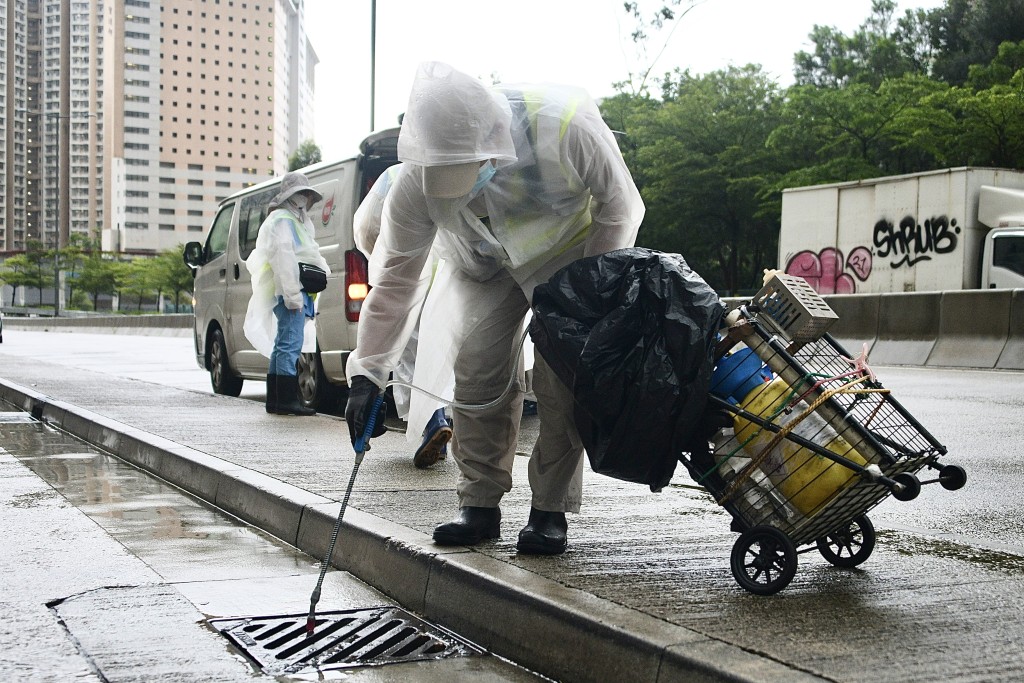 A person dressed in protective gear is collecting water samples or inspecting a street drain for Aedes mosquitoes as part of a public health response to chikungunya fever cases in Hong Kong in 2025.